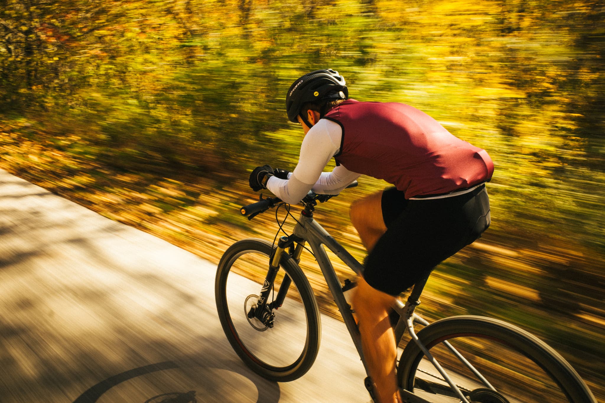 A cyclist in a helmet and sportswear riding a bike on a sunlit path surrounded by autumn foliage