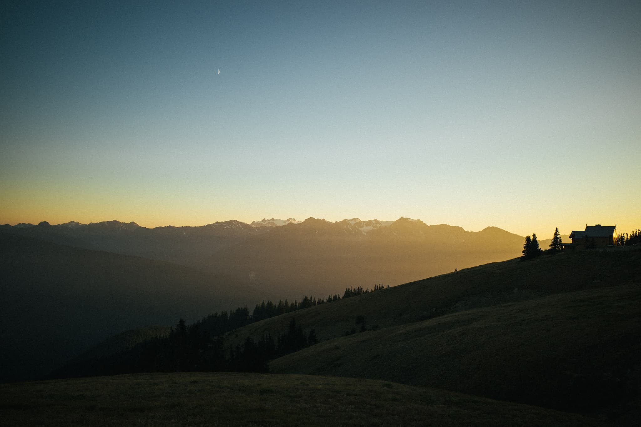 A serene sunset over a mountainous landscape with a silhouette of a small building on the right