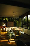 A cozy dining area bathed in warm sunlight with a wooden table, modern chairs, and large windows offering a view of greenery outside